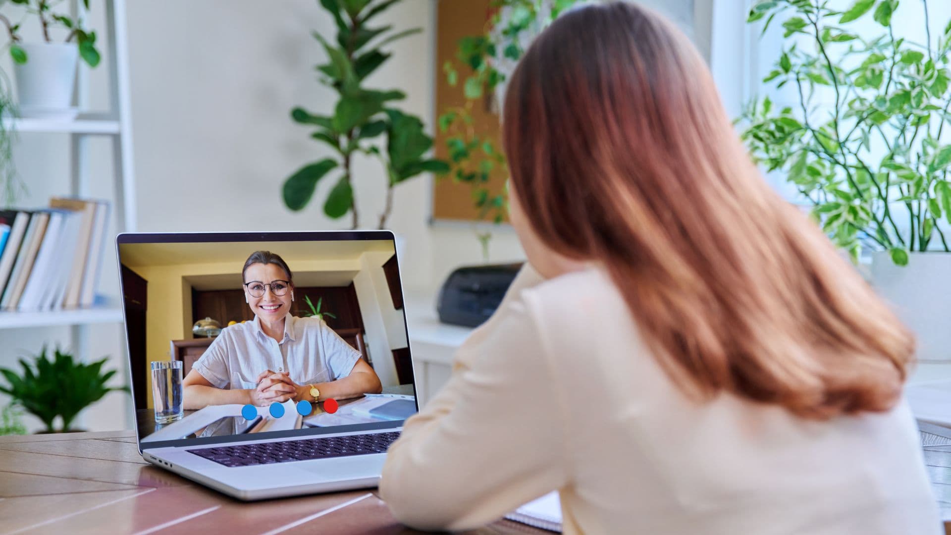 Frau bei einem Videocall am Laptop in einem hellen Raum mit Pflanzen.